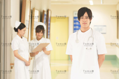 病院内に立つ若い男性医師と医療スタッフの画像