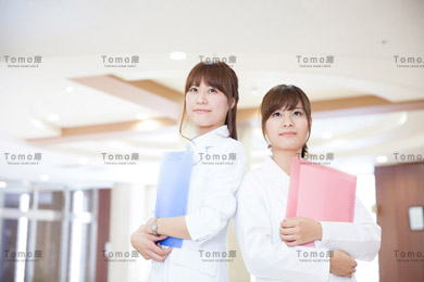 病院内で背中合わせに立ち上を見上げる女性医師2名の画像