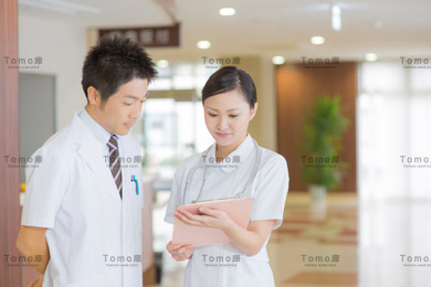 病院内で書類を見る男性医師と女性看護師（ナース）の画像