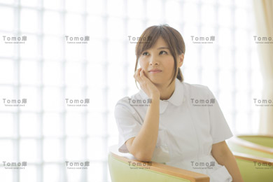 病院内で椅子に座り考え事をする女性看護師（ナース）の画像