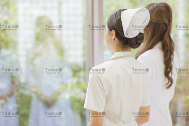 病院内から外を見る女性医師と女性看護師（ナース）の後姿の画像