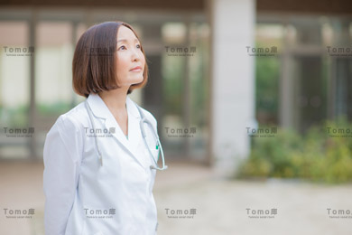 病院の中庭で上を見上げる女性医師の画像