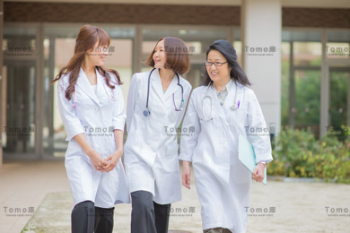 病院の中庭を歩く女性医師3名の画像