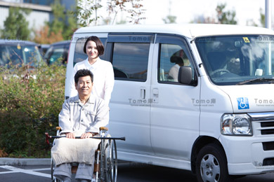 駐車場の車椅子の患者と女性看護師の画像