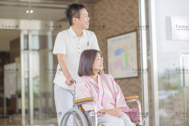 病院内を移動する車椅子の女性患者と男性医療スタッフの画像