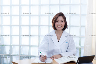 笑顔で書類を書く女性医師の画像