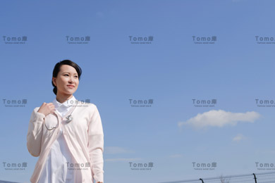 青空を背景に立つ女性看護師（ナース）の画像