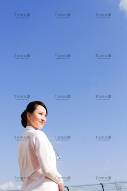 青空を背景に立つ女性看護師（ナース）の画像