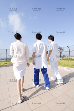 病院の屋上を歩く男性医師2名・女性看護師の後姿の画像