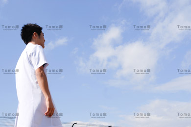 青空を背景に立つ若い男性医師の画像